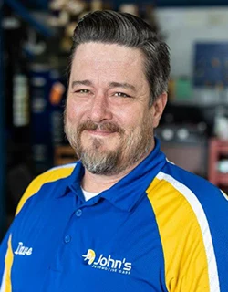 Man in blue and yellow work shirt with logo, smiling, indoors.