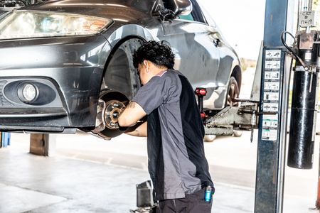 Mechanic works on a car tire, vehicle raised on a lift. Shop setting with equipment.