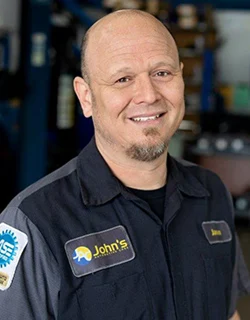 Man in mechanic uniform smiling at camera. John's Auto Repair shop.