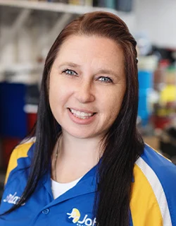 Woman with blue eyes and dark hair smiling, wearing a blue and yellow uniform in a store setting.