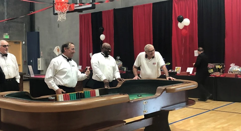 Casino event with people around a roulette table. Black, red, and white decor. People in formal attire.