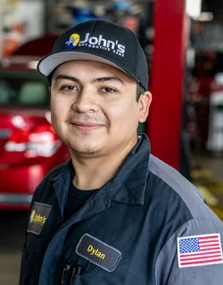 Mechanic Dylan in work uniform smiles at camera in auto repair shop.