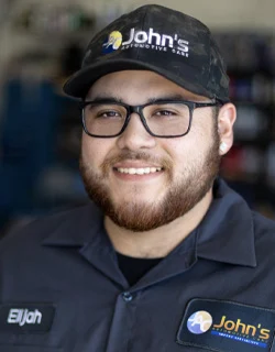 Man in John's Automotive Care uniform smiling, wearing glasses and hat, badge reads 
