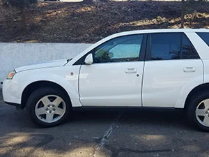 White Saturn SUV parked on a paved surface next to a white wall.