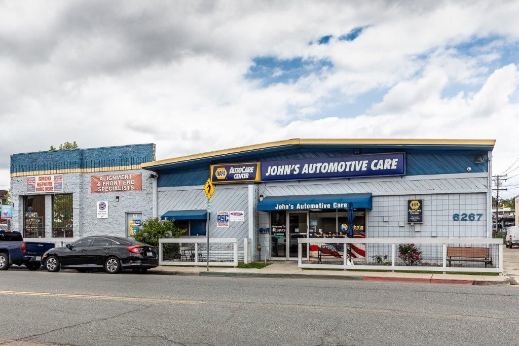 John's Automotive Care building with blue awning, parked cars, and cloudy sky.