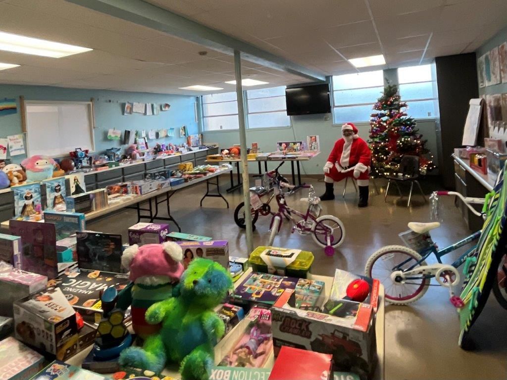A room with toys and a seated Santa near a Christmas tree.
