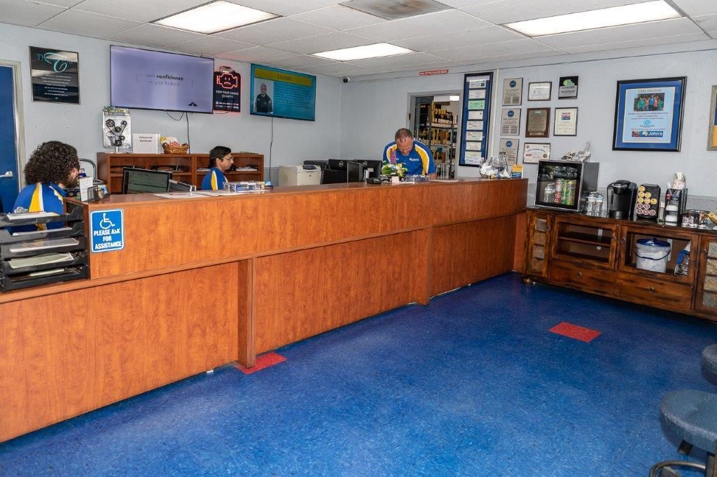 Inside of auto shop with blue floor, brown counter, and three people wearing blue and gold shirts behind it.