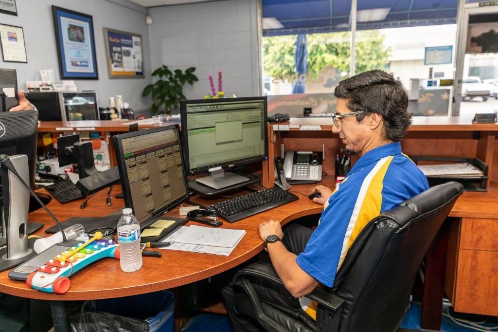 Man in blue shirt works at a desk, facing two computer monitors, in an office.