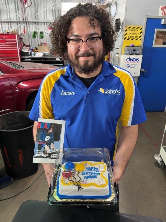 Man holding a birthday cake and a photo in a garage. Cake has 