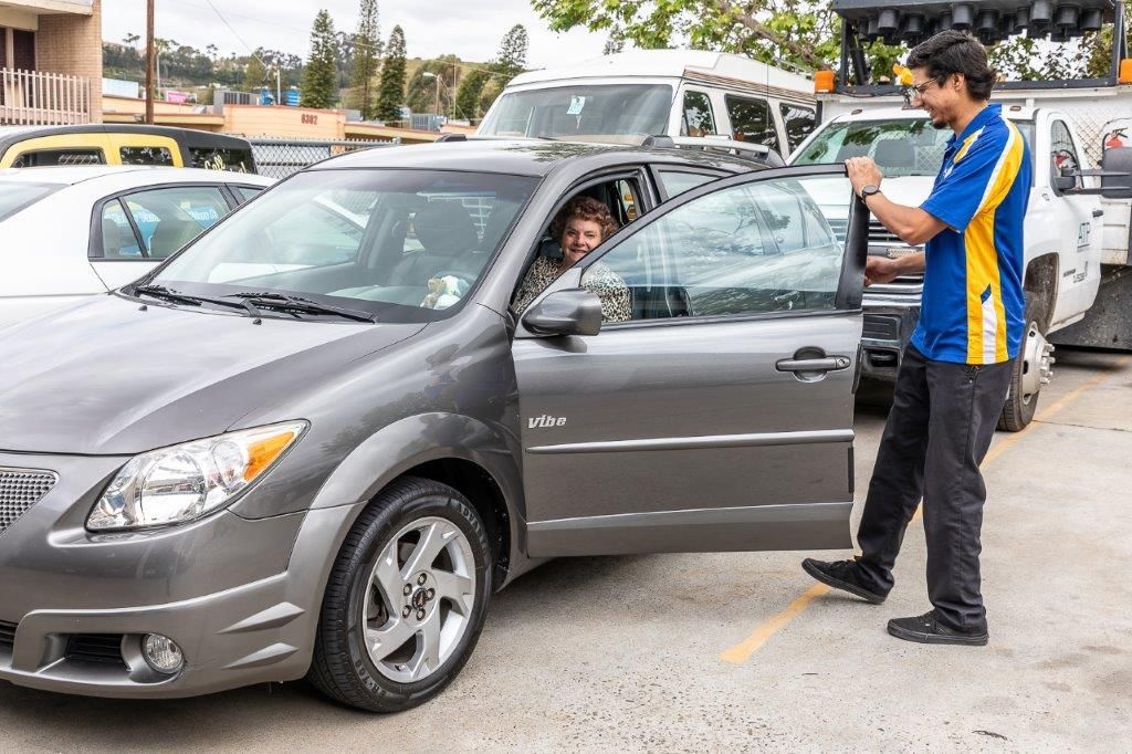 Man helping a driver exit a gray car in a parking lot.