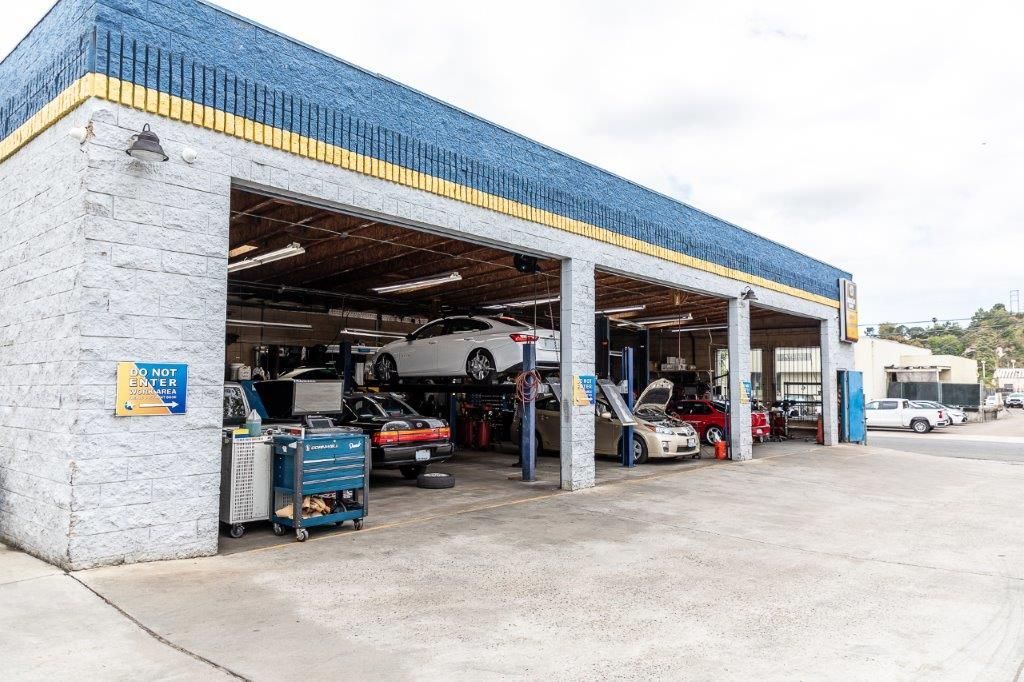 Auto repair shop exterior with cars on lifts, various vehicles inside and outside. Blue and yellow trim.