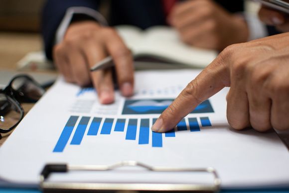 Hands pointing at a bar graph on a paper, likely reviewing financial data.