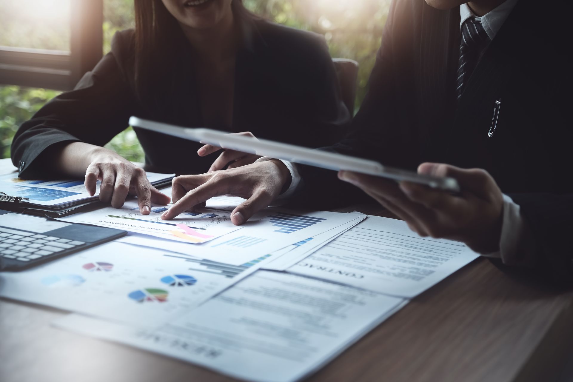 Two people in business attire reviewing financial documents, pointing at charts, and using a tablet.