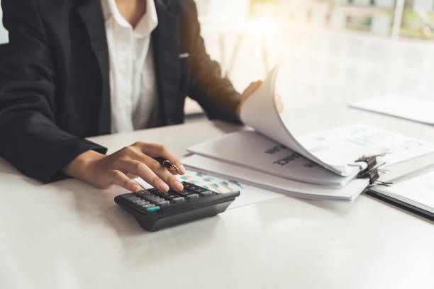 Person in a suit calculating with a calculator, reviewing documents at a desk.