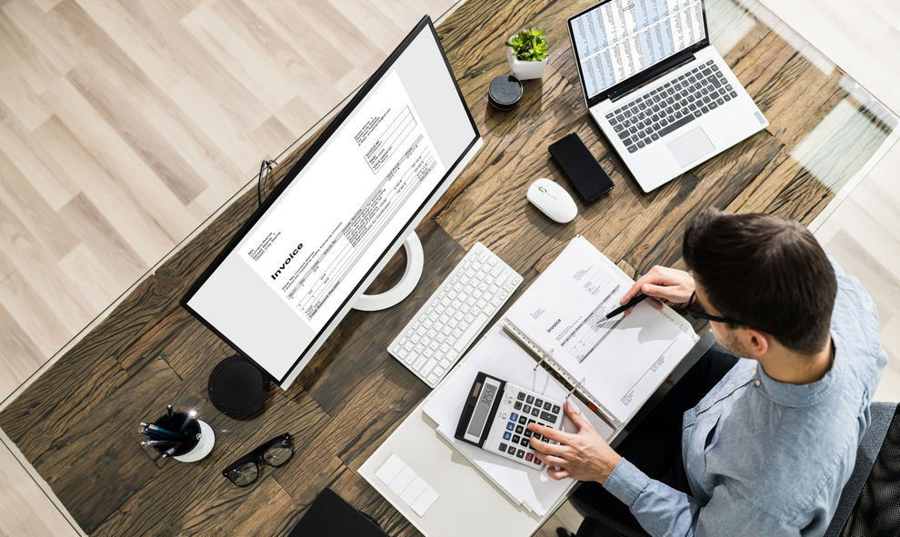 Man working on finances at desk with computer, calculator, and documents. Man working on finances at desk with computer, calculator, and documents.