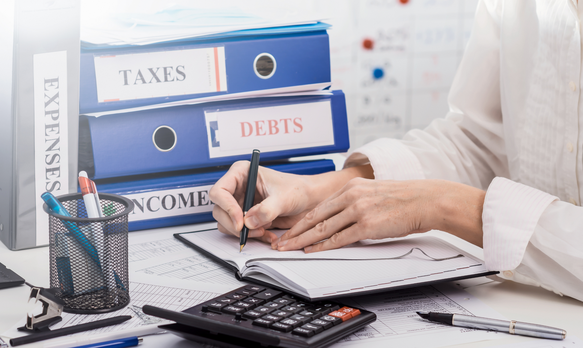 Person writing in notebook at desk with binders labeled 