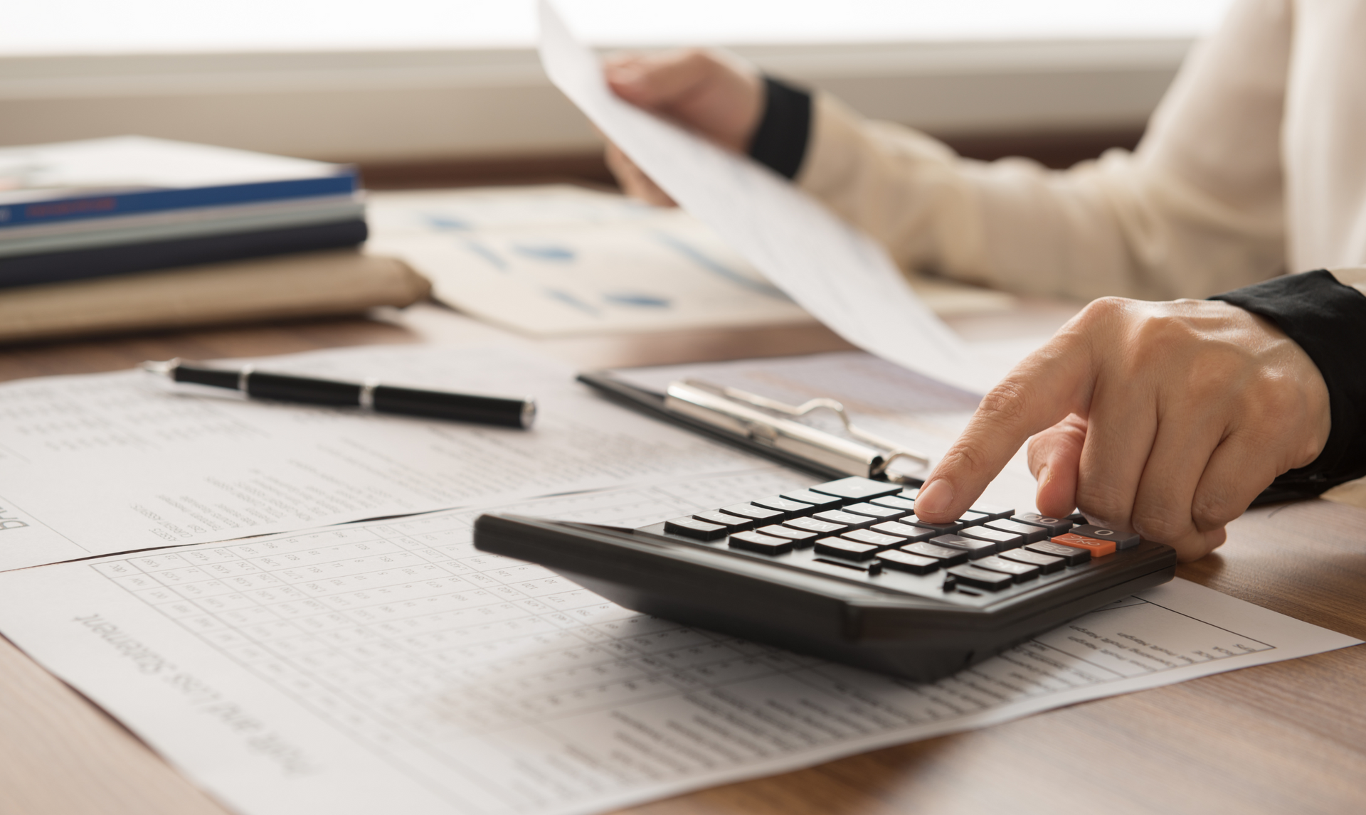 Person using a calculator while reviewing papers on a desk. Person using a calculator while reviewing papers on a desk.