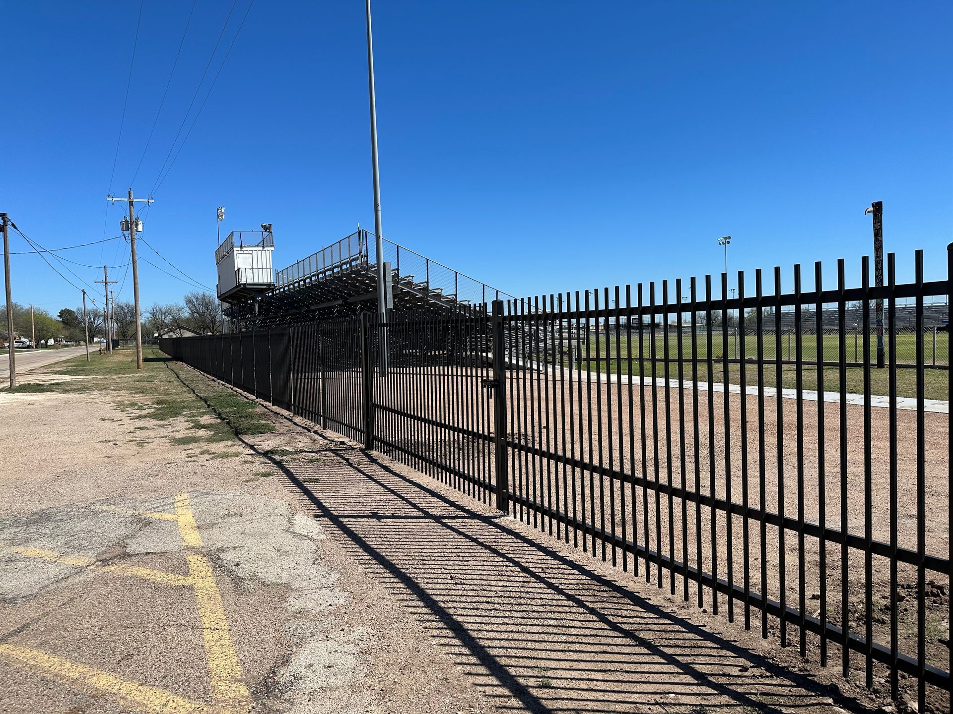 A black metal fence surrounds a dirt field with a bleacher in the background.