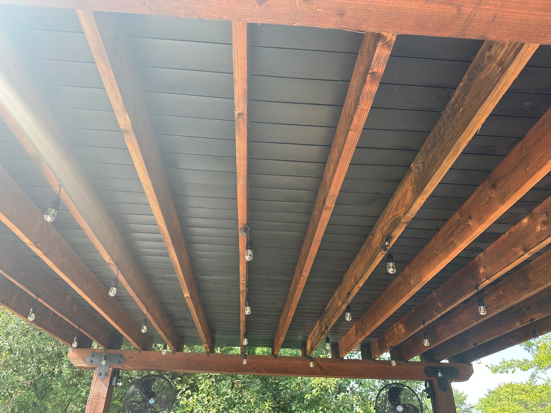 The ceiling of a wooden pergola with lights hanging from it.
