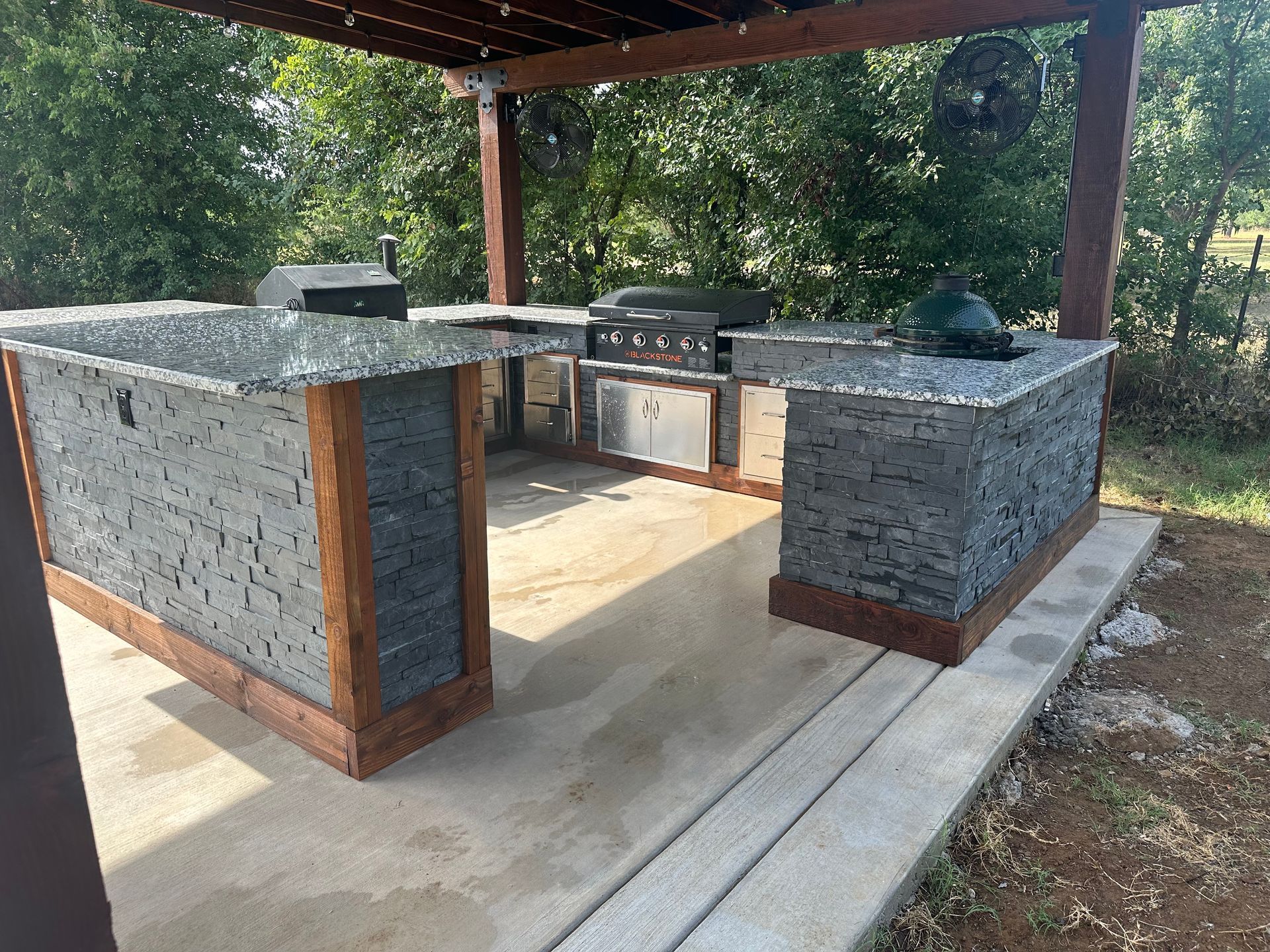 A large outdoor kitchen with a grill and sink under a pergola.