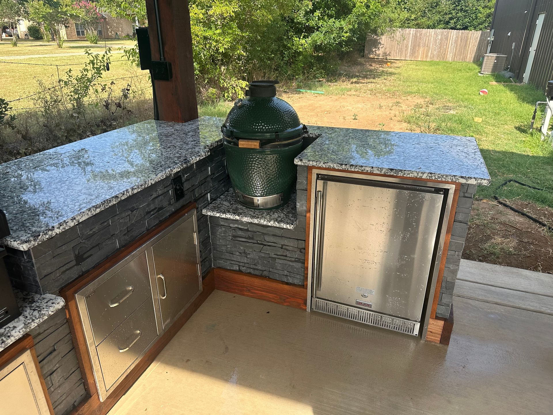 A large green egg is sitting on top of a granite counter in an outdoor kitchen.