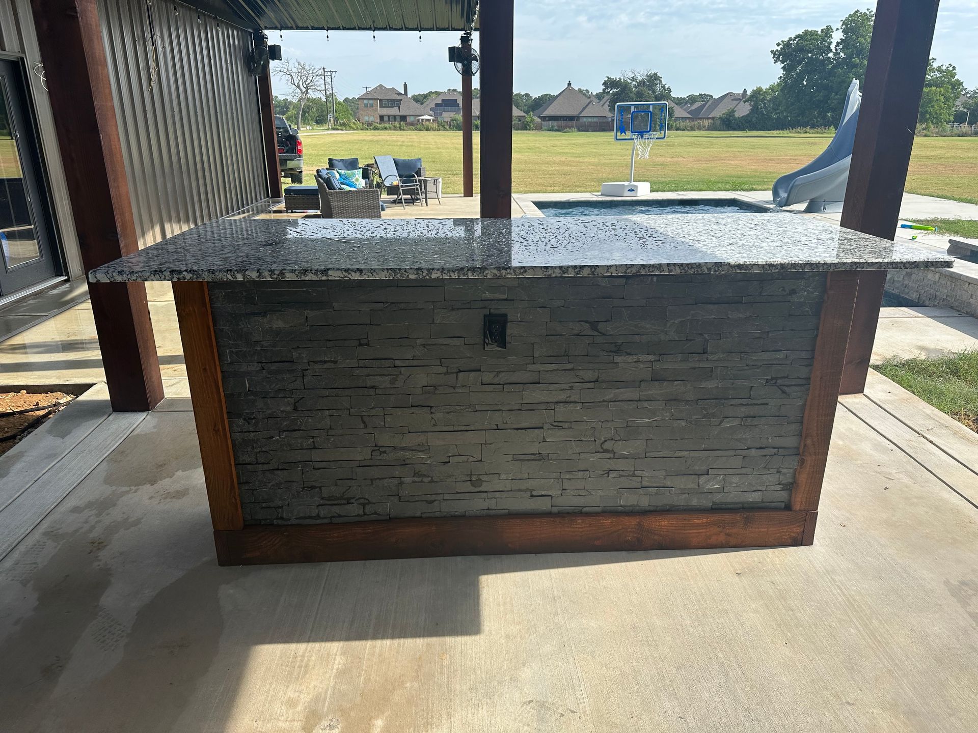 A large granite counter top is sitting on top of a concrete patio next to a pool.