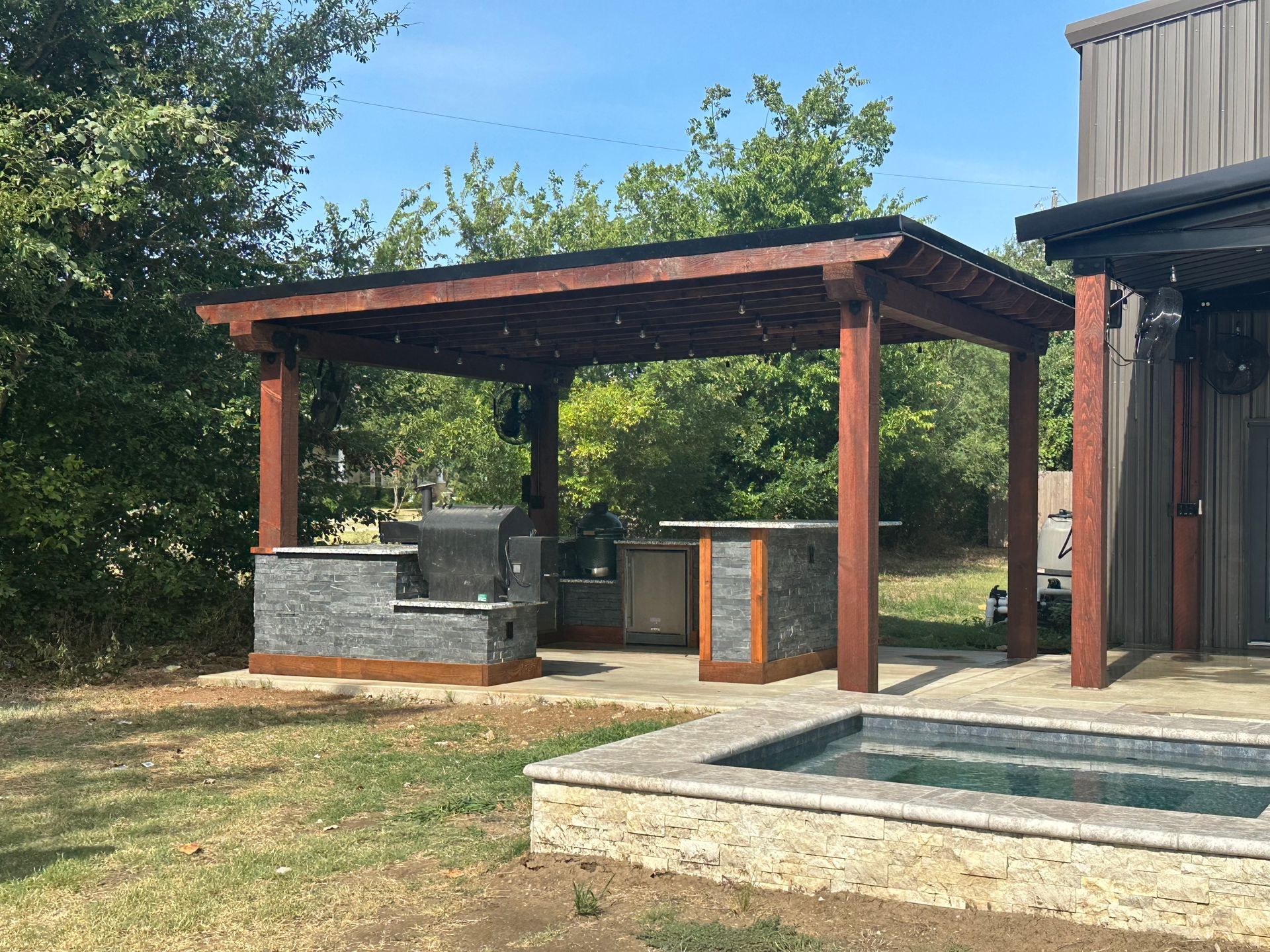 A pergola with a grill and a pool in the backyard of a house.