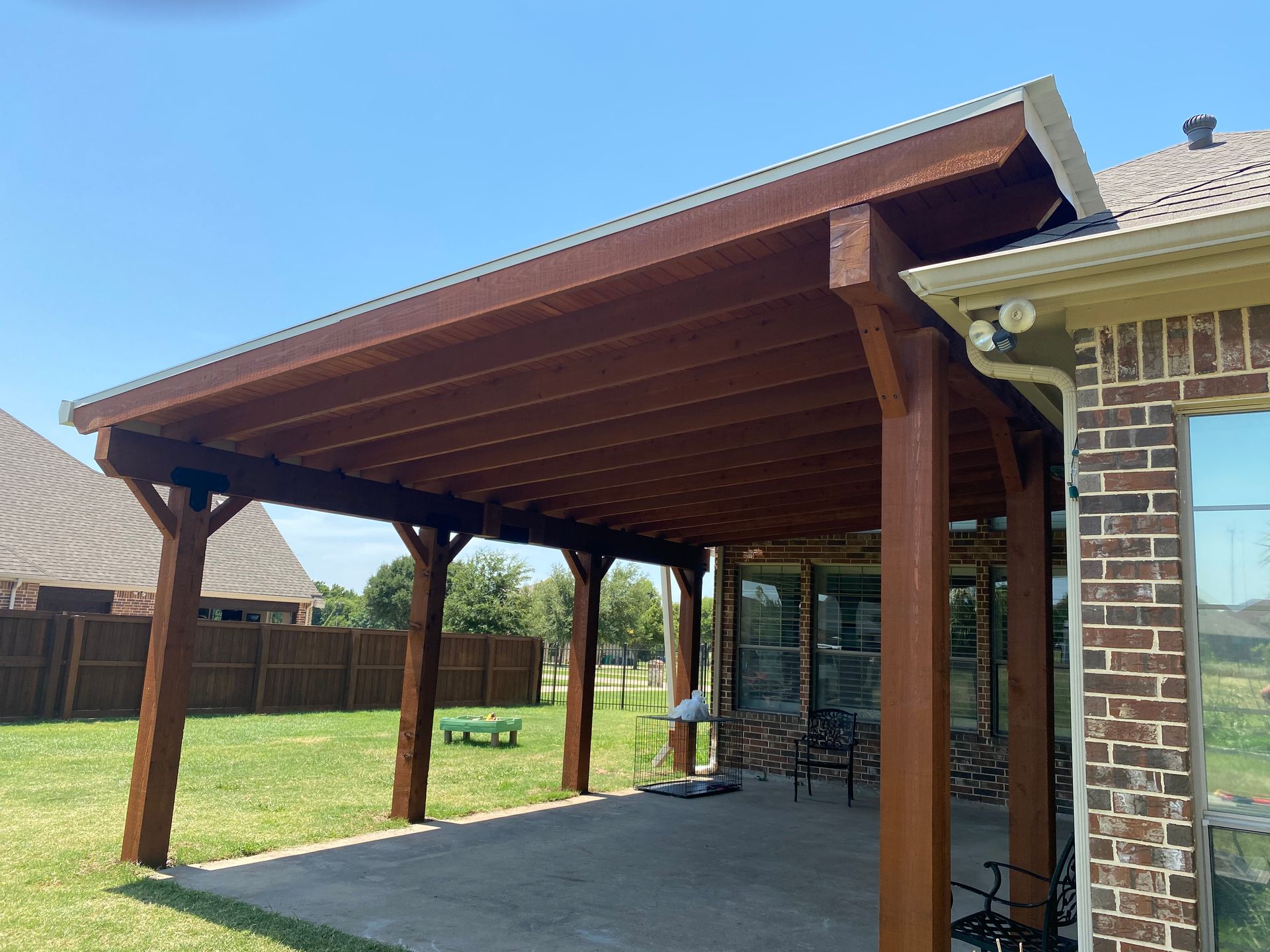 A wooden pergola is sitting on the side of a brick house.