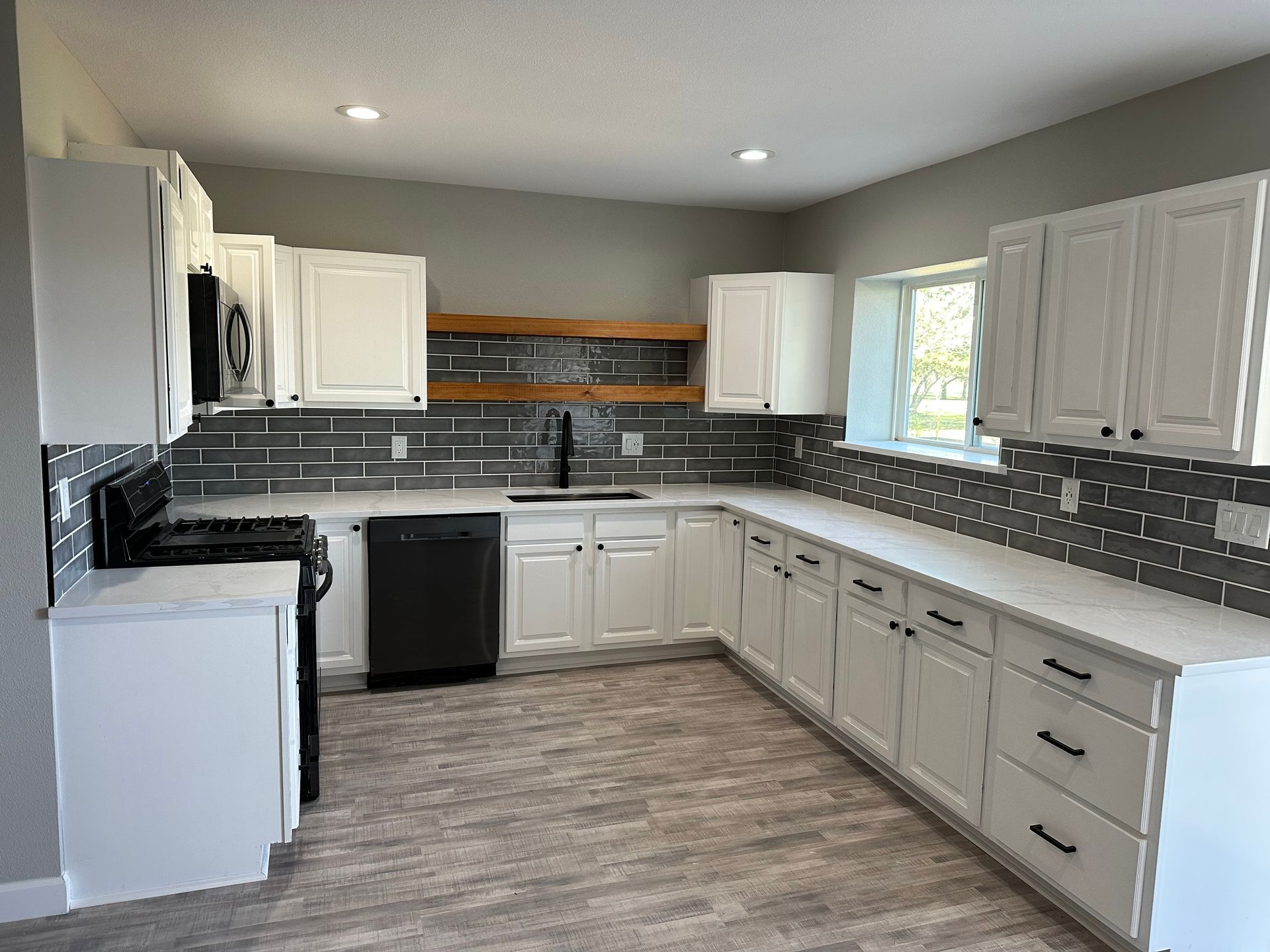 A kitchen with white cabinets , black appliances , and a window.