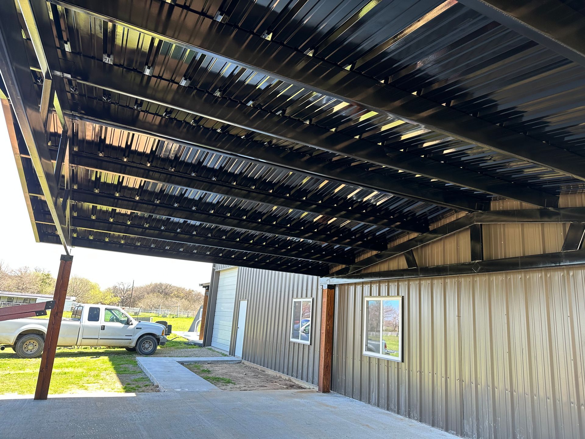 A white truck is parked under a black roof in front of a building.