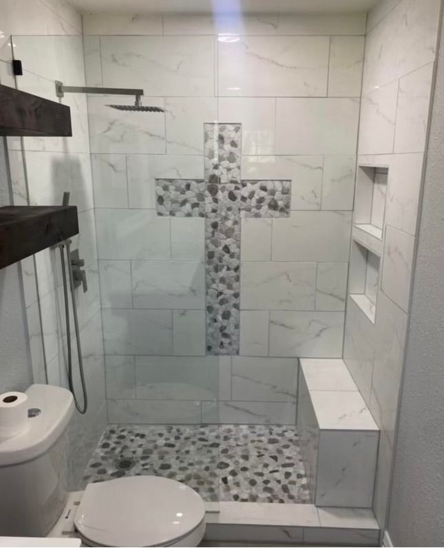 A bathroom with a toilet and a walk in shower with a cross on the wall.