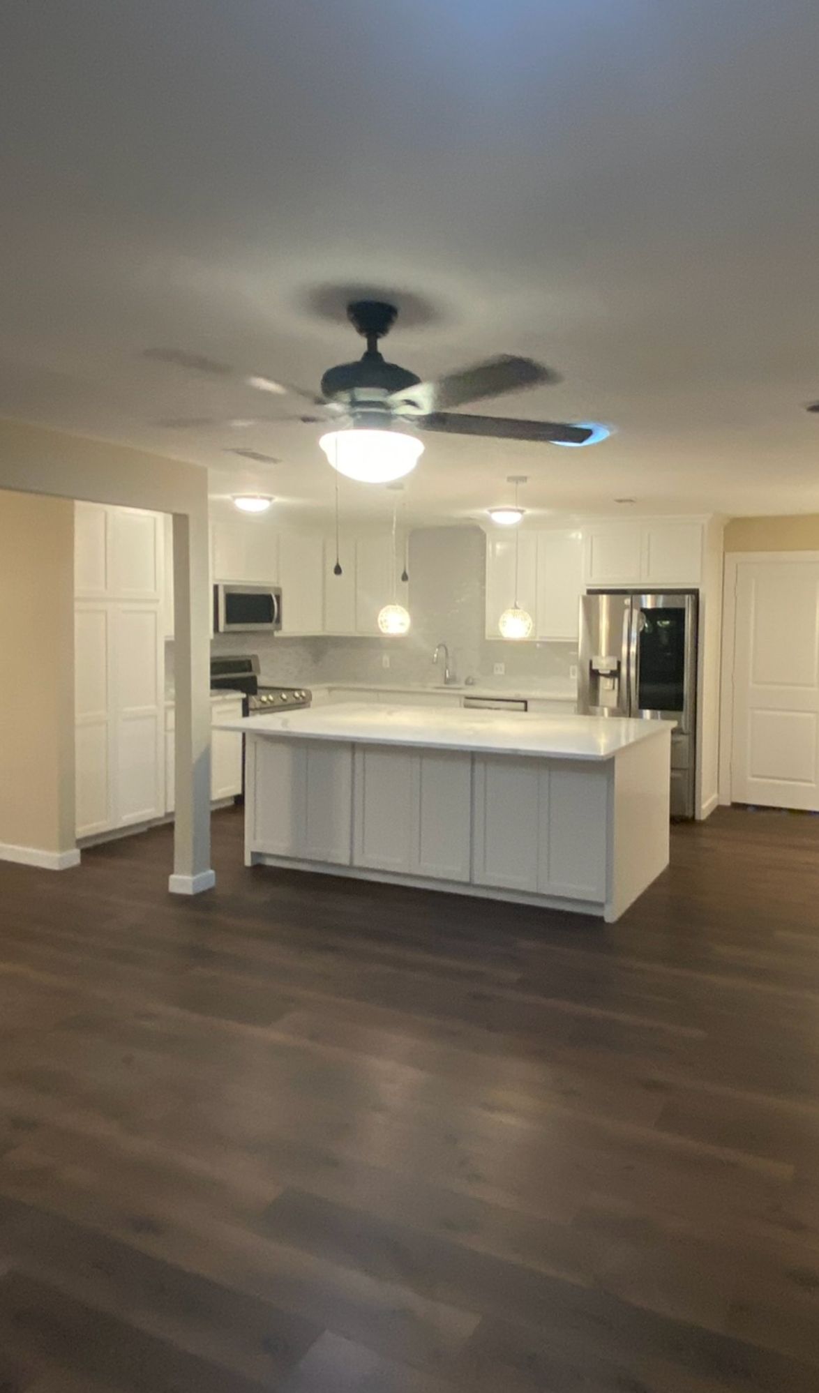 An empty kitchen with a large island and a ceiling fan.