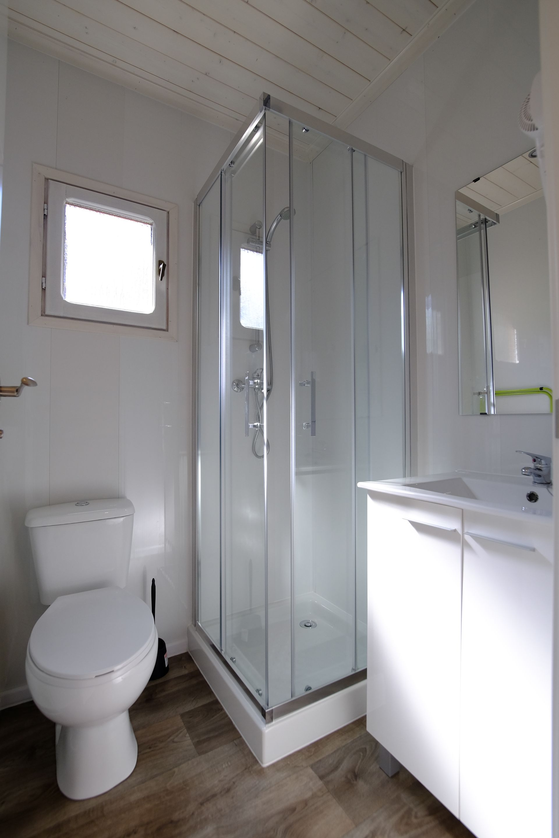 Baño pequeño y blanco con ducha de cristal, inodoro y lavabo.