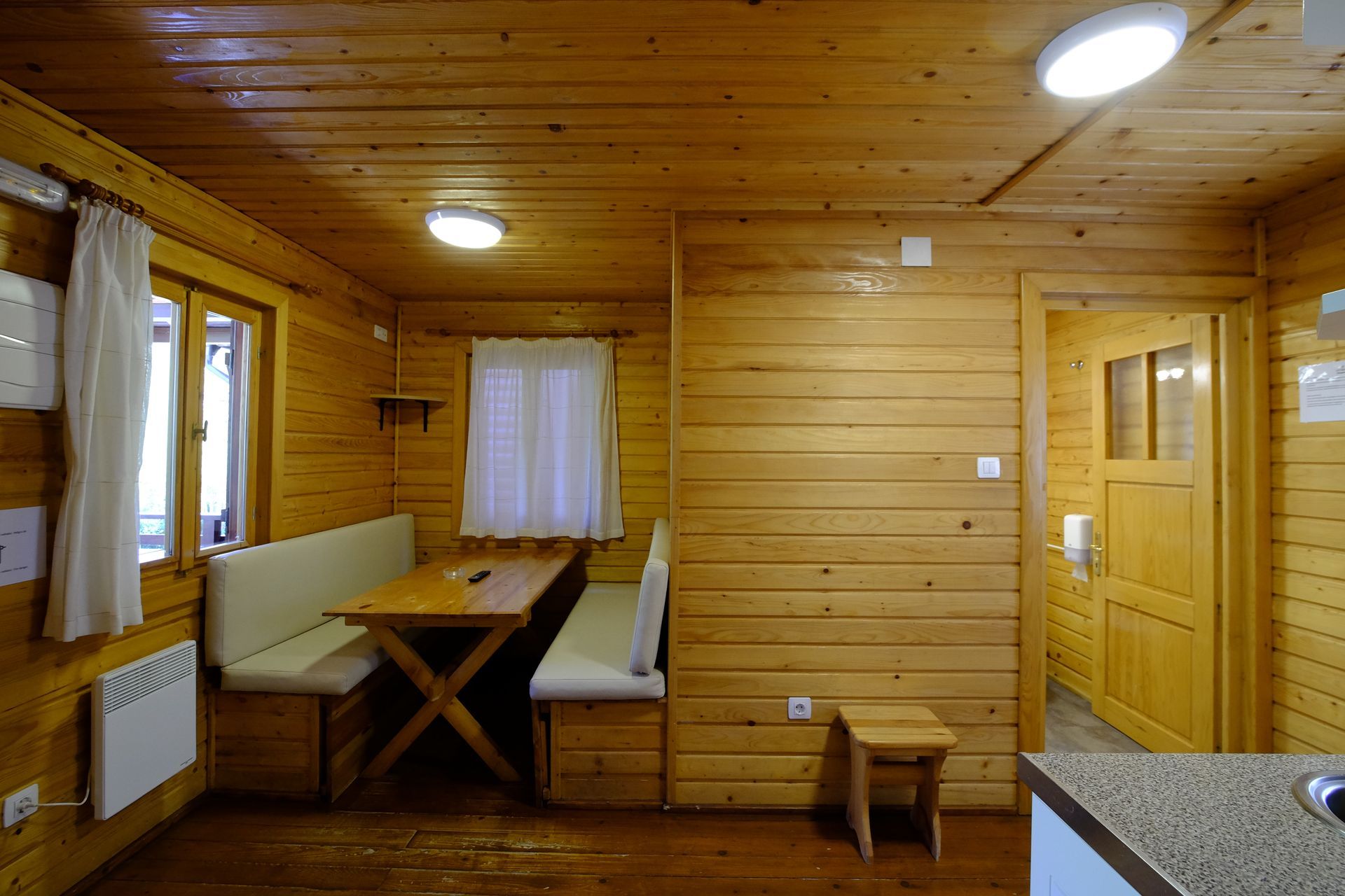 Interior de una cabaña de madera con mesa de comedor, bancos y puerta.