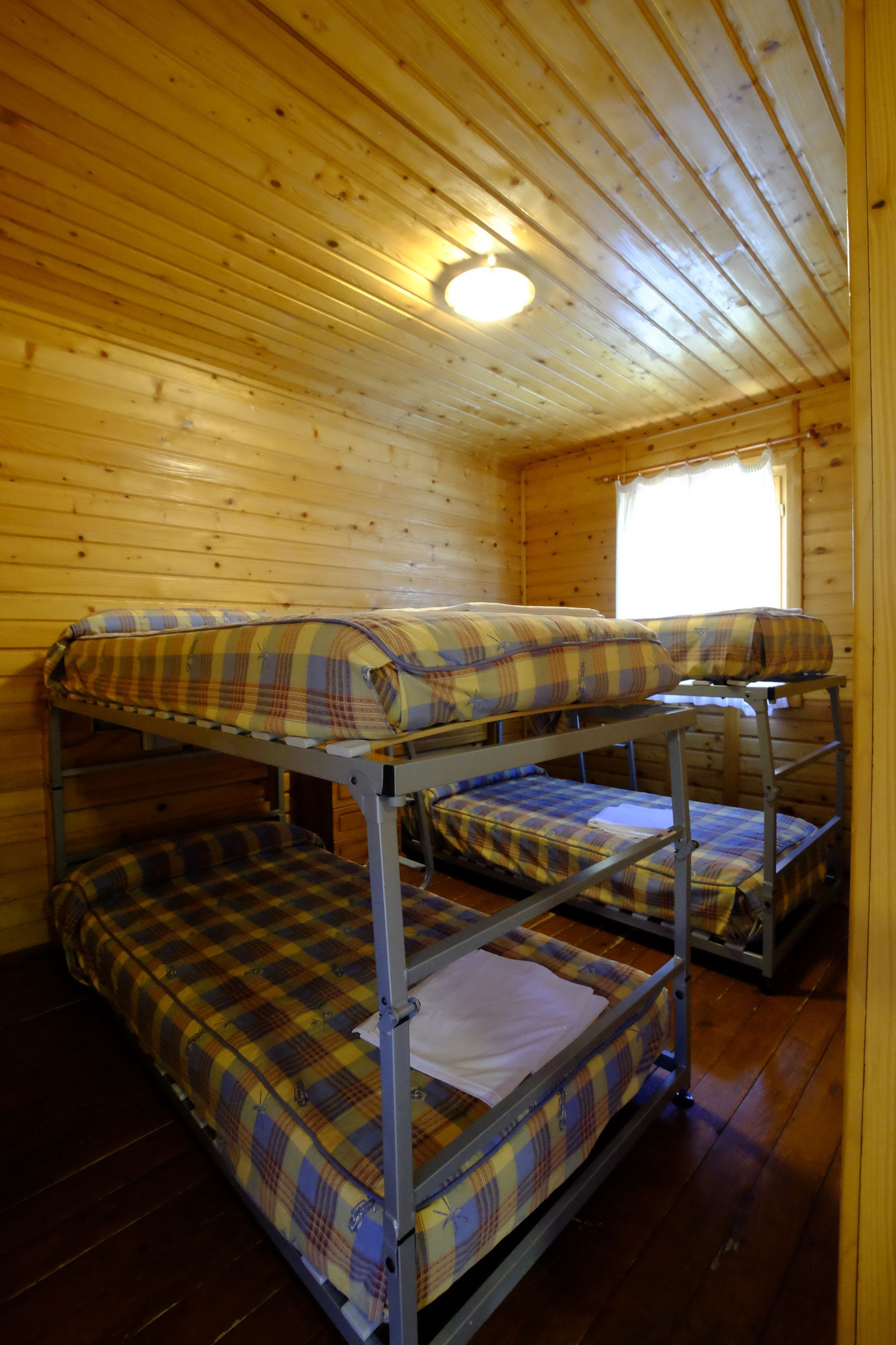 Habitación con paneles de madera, dos literas y una cama individual. La luz entra por una ventana.