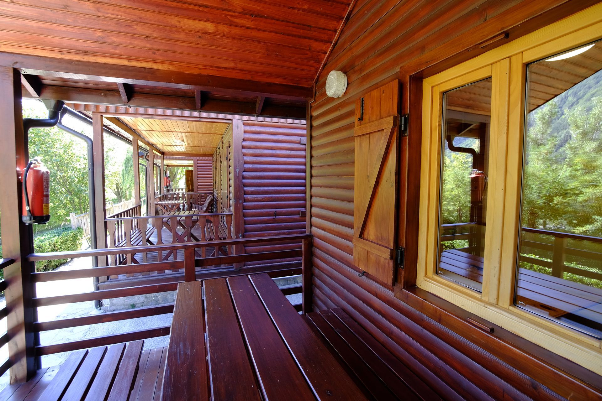 Exterior de cabaña de madera con porche y contraventanas, mesa y sillas.