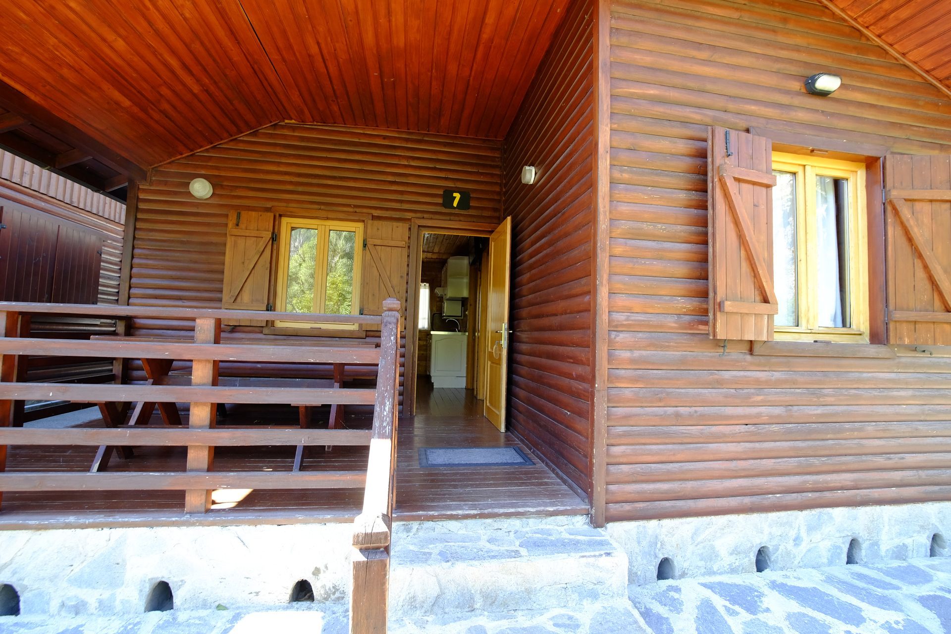 Exterior de cabaña de madera con porche, escalones y puerta delantera abierta.