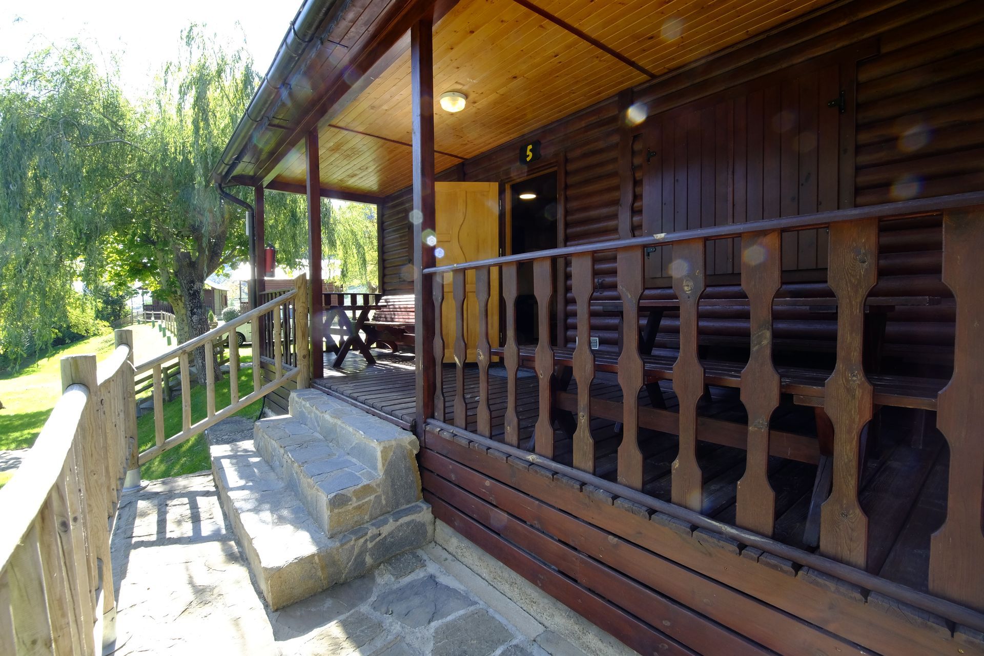 Cabaña de madera con porche, escaleras y barandilla.