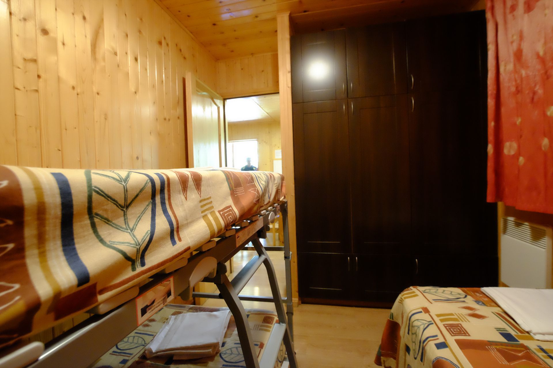 Interior de un dormitorio en una cabaña de madera con literas, un armario y una cama individual; tonos cálidos.