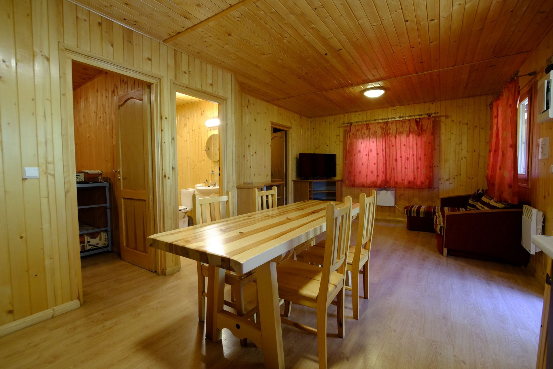 Interior con paneles de madera, mesa y sillas de comedor, que da a las puertas. Luz natural, cortinas rojas.