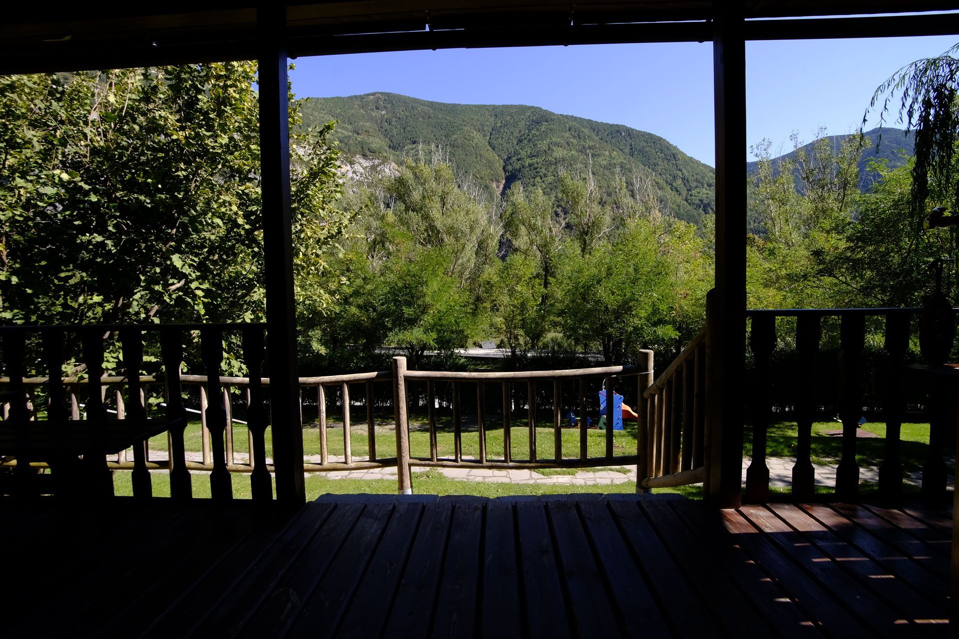 Porche de madera con vistas a una sierra y árboles en un día soleado.