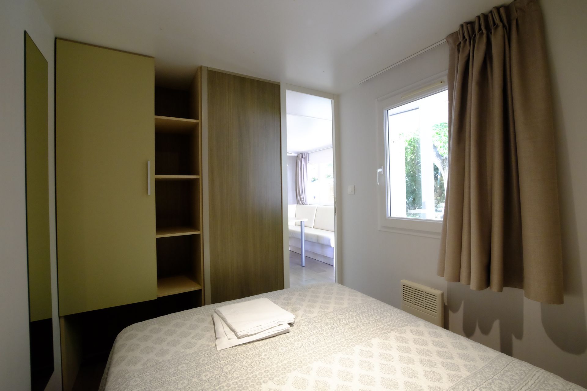 Dormitorio con cama, armario, ventana y una vista parcial a otra habitación.