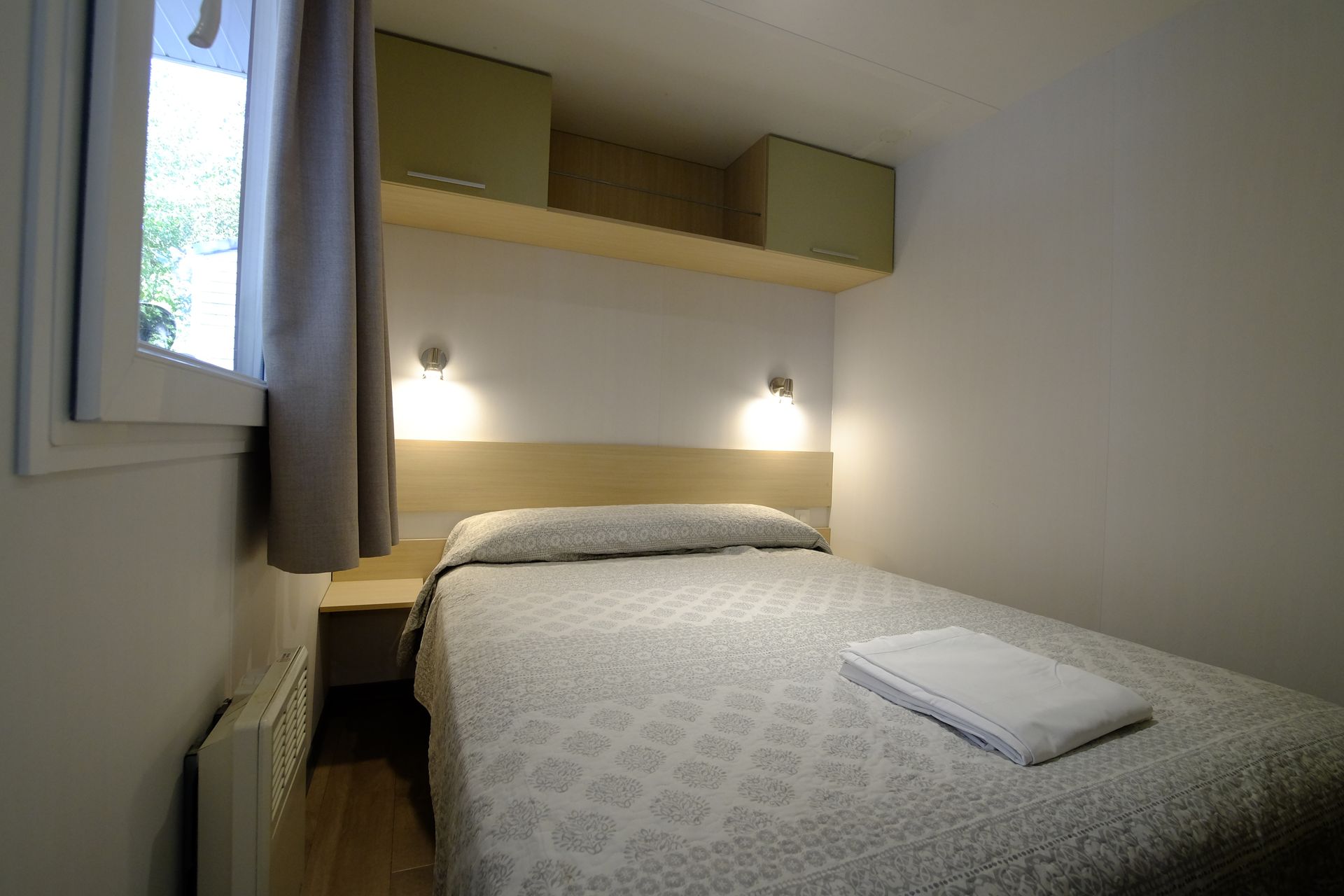 Dormitorio pequeño y sencillo con una cama, una ventana pequeña y espacio de almacenamiento arriba.