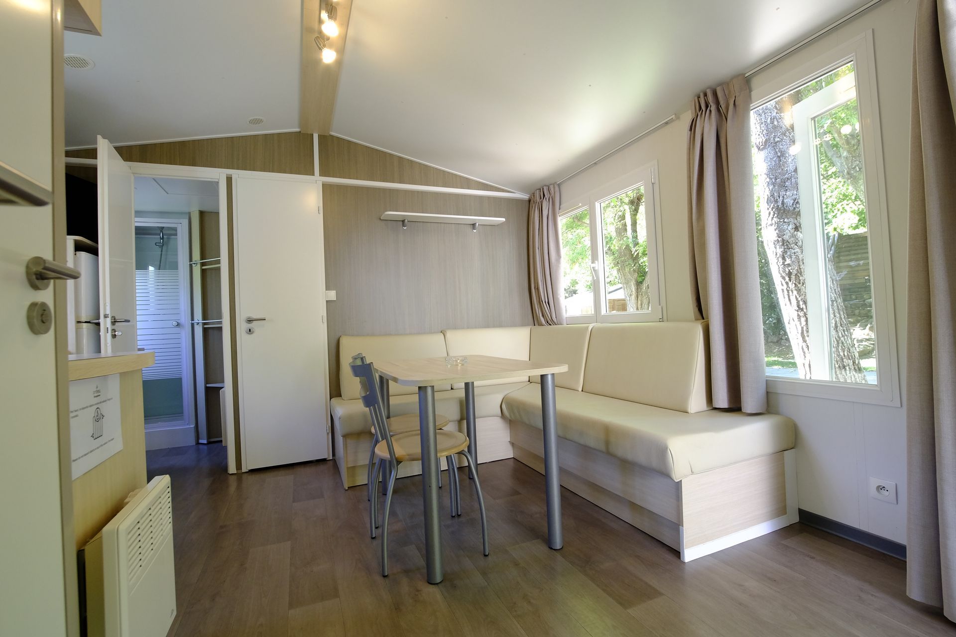 Interior de una casa móvil con una mesita, un sofá empotrado y vistas al exterior a través de las ventanas.