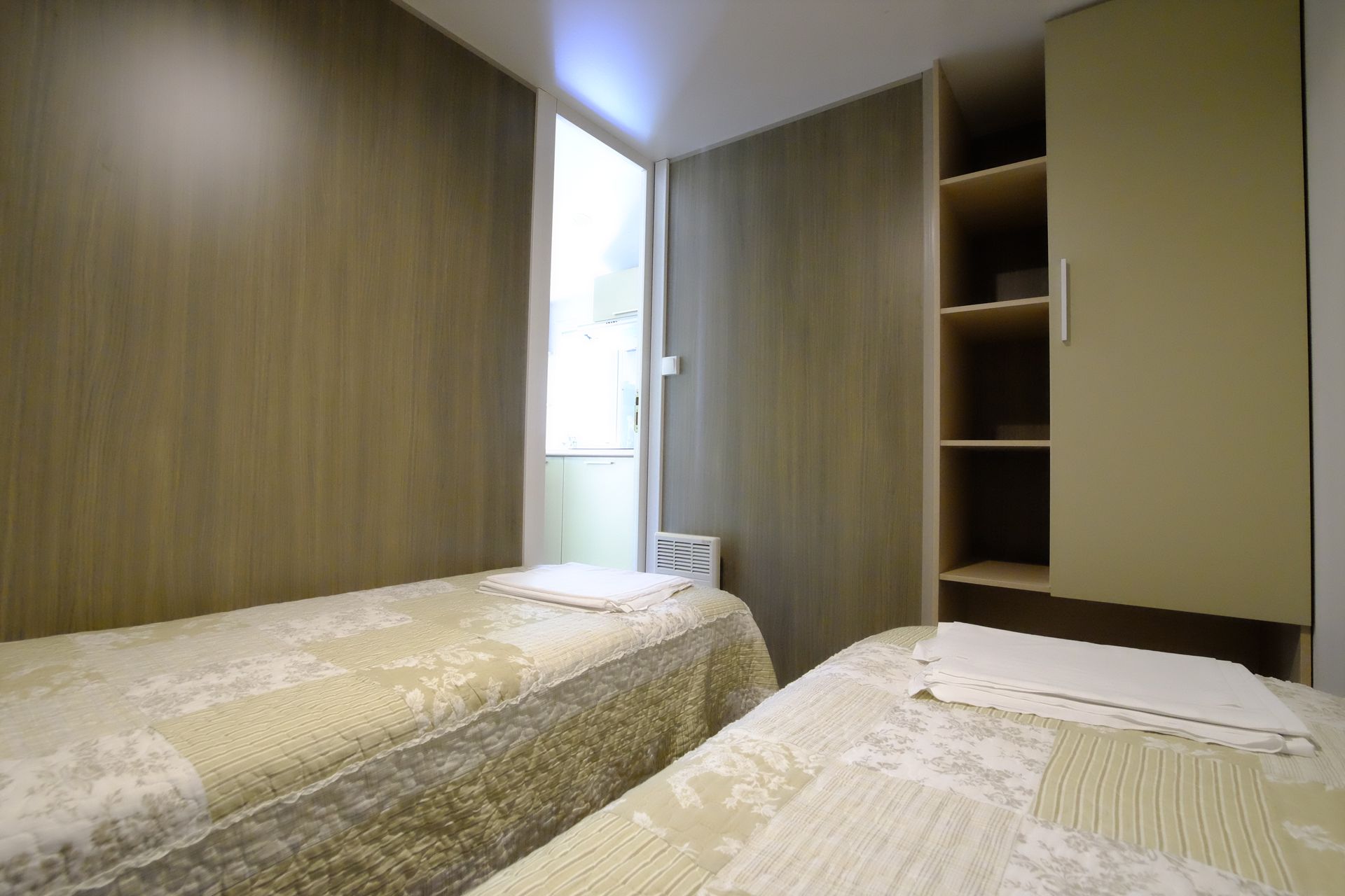 Dos camas individuales en una habitación pequeña con un armario abierto y una puerta que da al exterior.