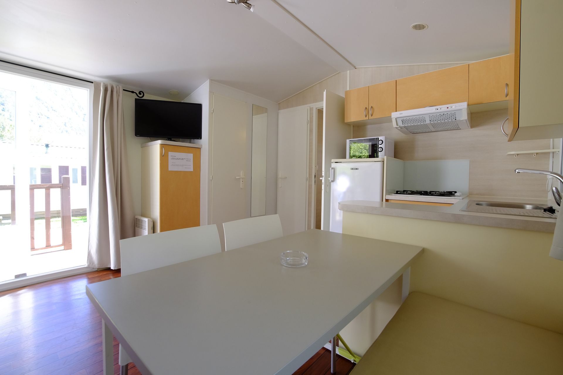 Interior de una pequeña casa de vacaciones: cocina, comedor y televisión. Luminosa, espaciosa, con una puerta corredera.