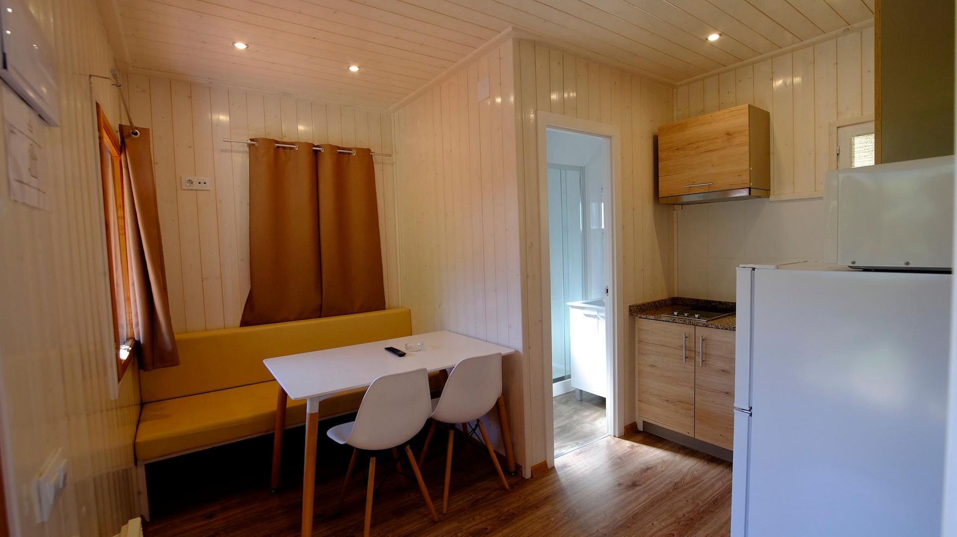 Interior de una pequeña cabaña con cocina, comedor y puerta a otra habitación.