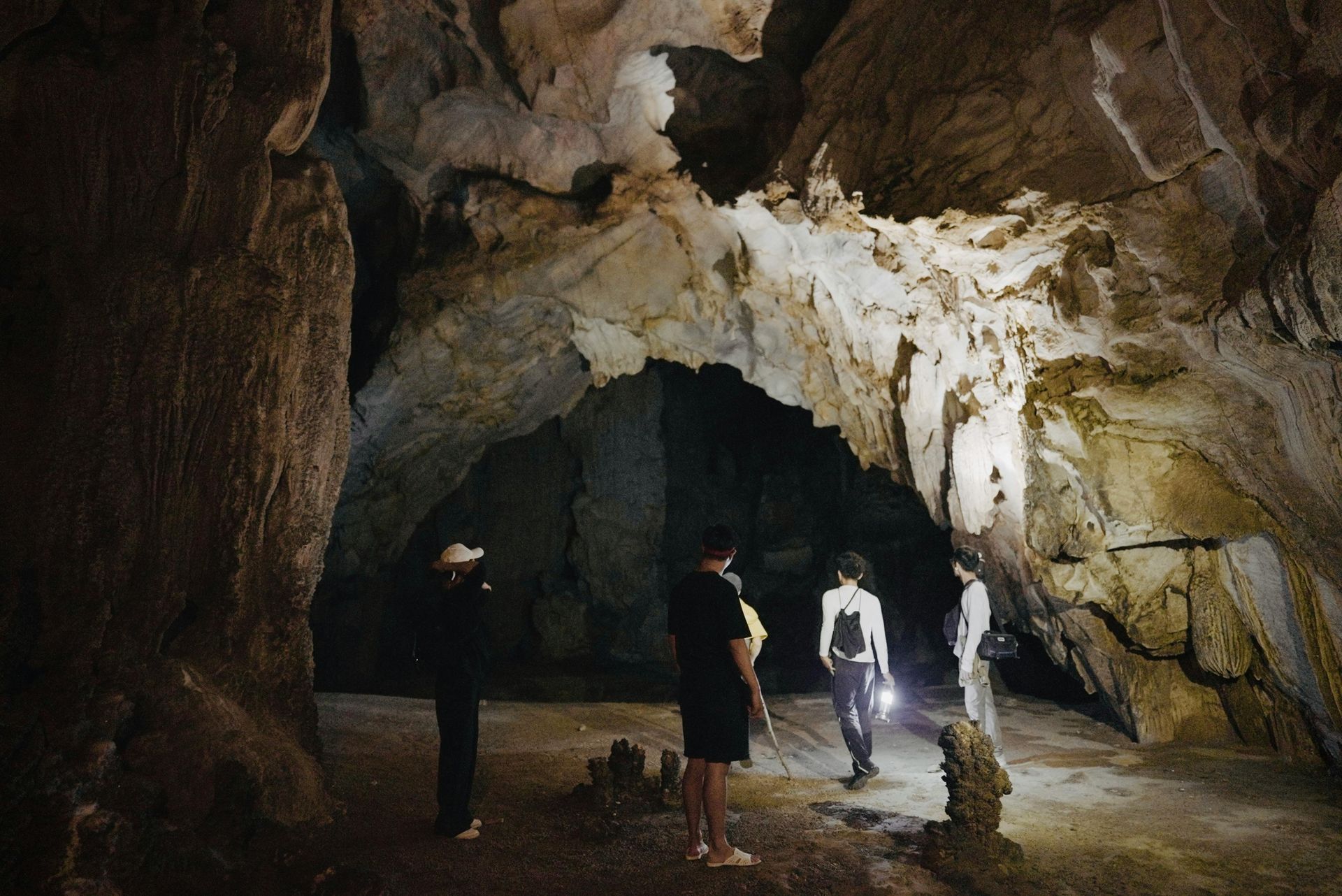 Personas explorando una cueva tenuemente iluminada, utilizando linternas para iluminar las formaciones rocosas.