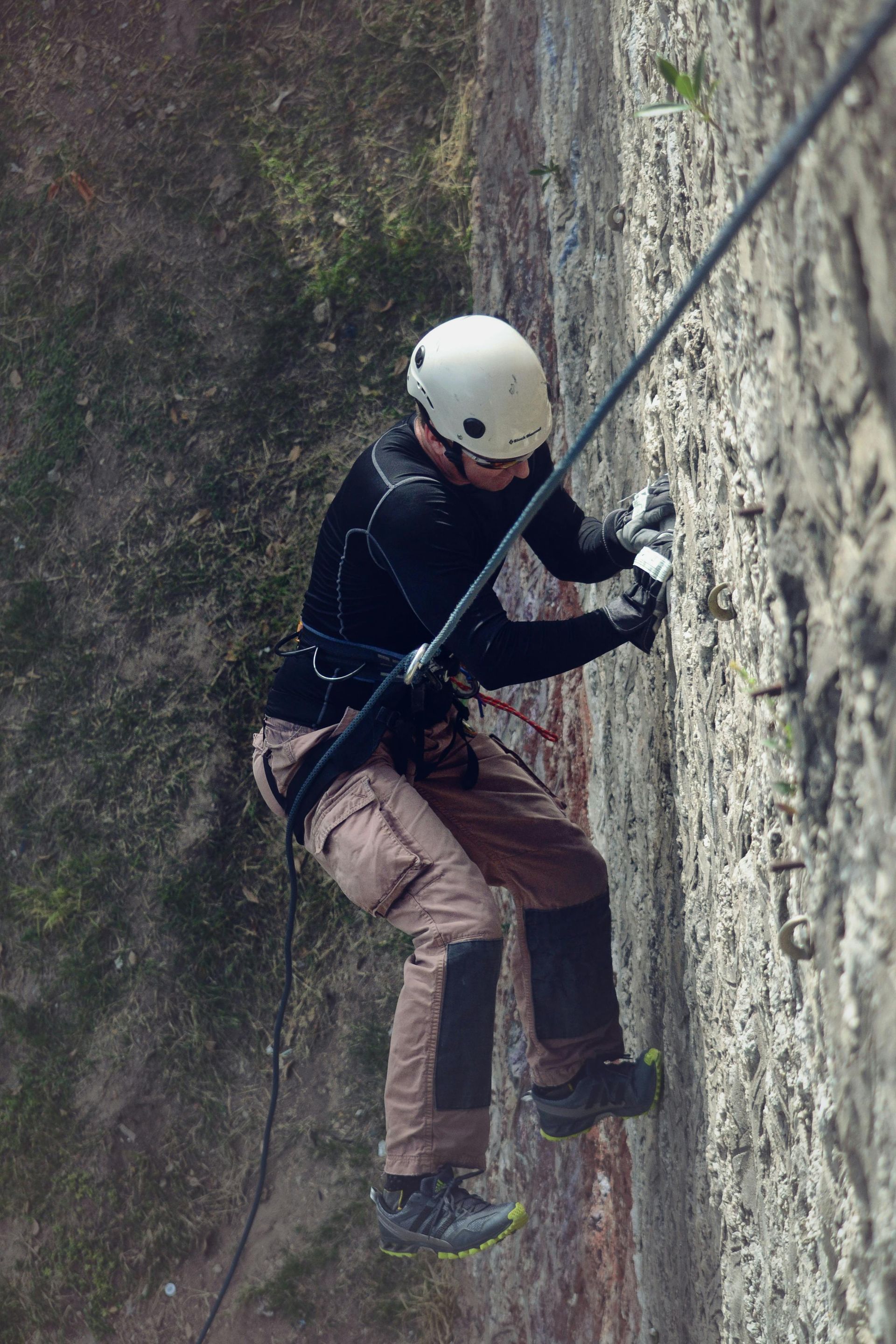 Persona descendiendo en rápel por una pared de piedra, con casco y equipo de escalada.