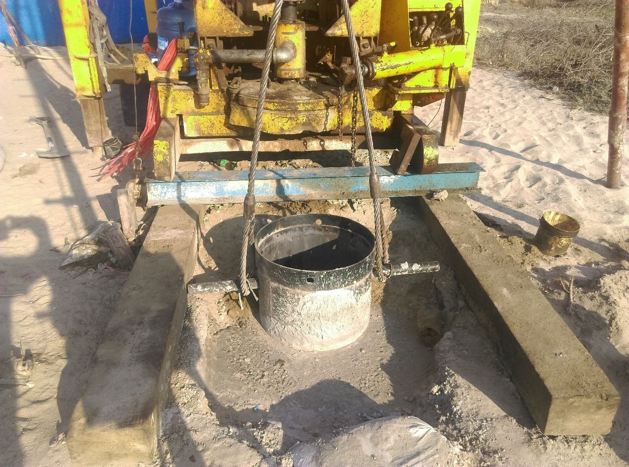 Plataforma de perforación de pozos extrayendo tierra de un agujero en el suelo. Máquina amarilla, entorno arenoso.